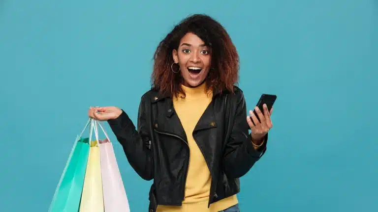 Excited young woman holding shopping bags and a smartphone