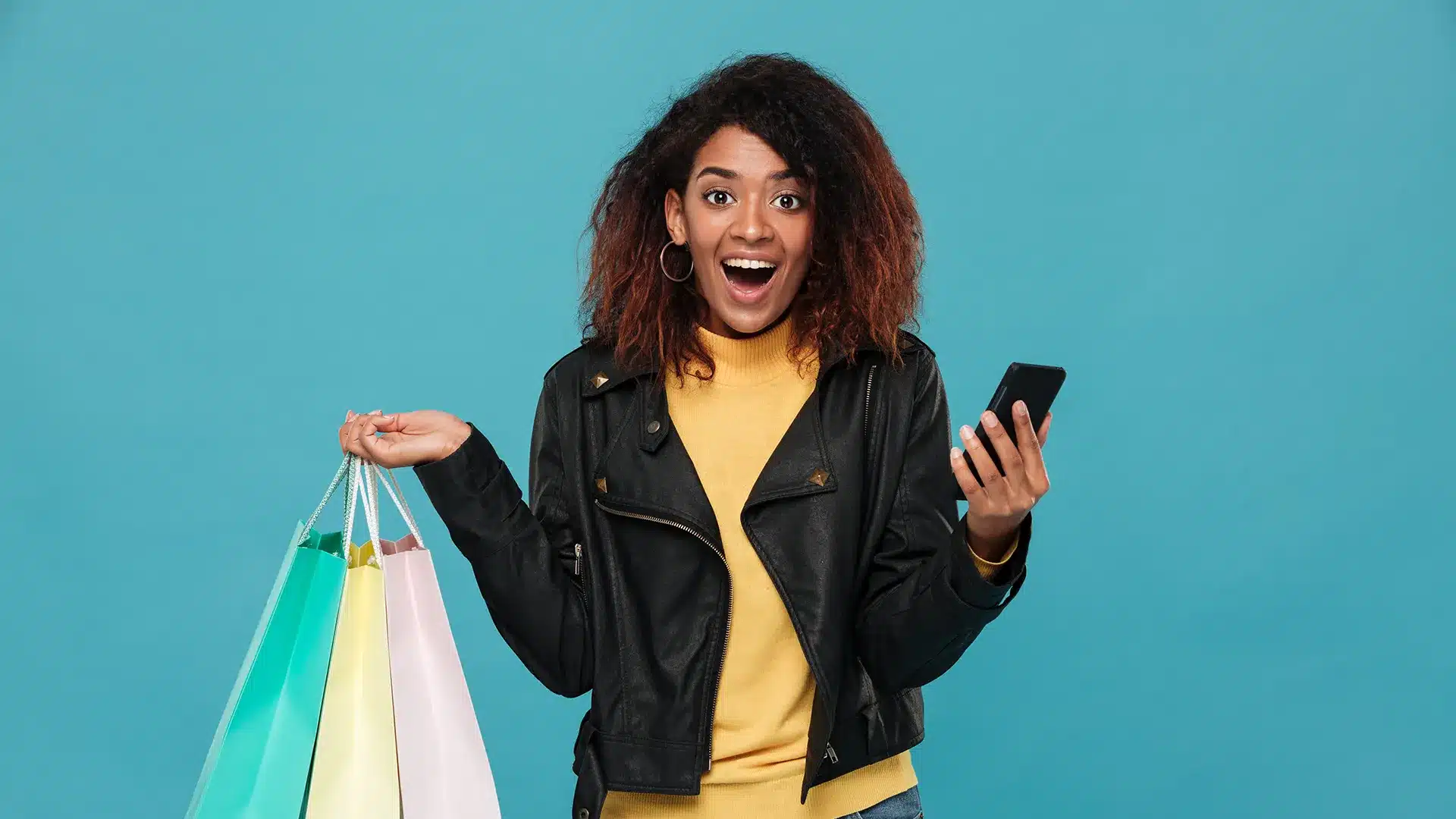 Excited young woman holding shopping bags and a smartphone