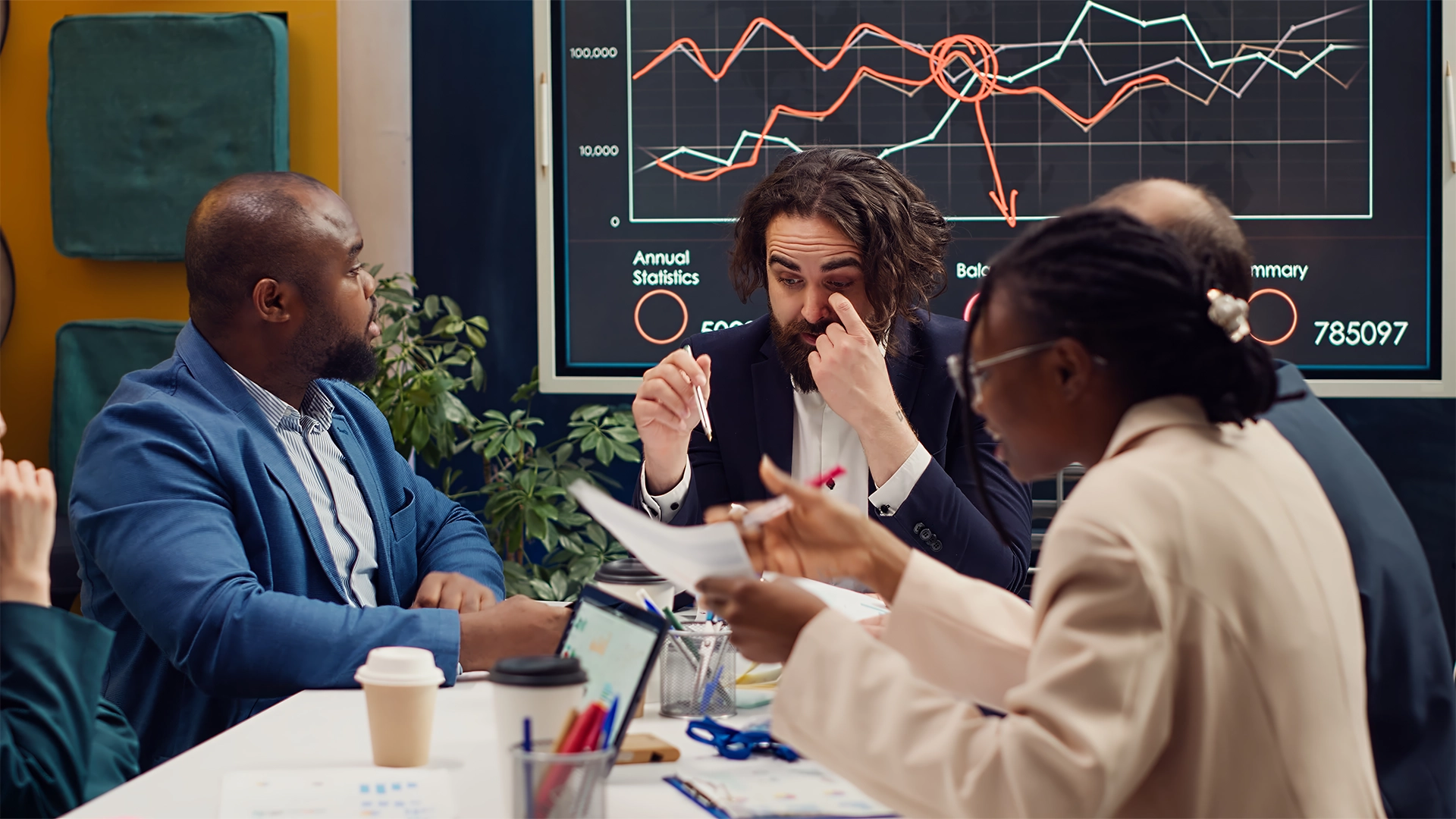 Business team in a conference room analyzing declining financial graphs on a screen during a strategy meeting