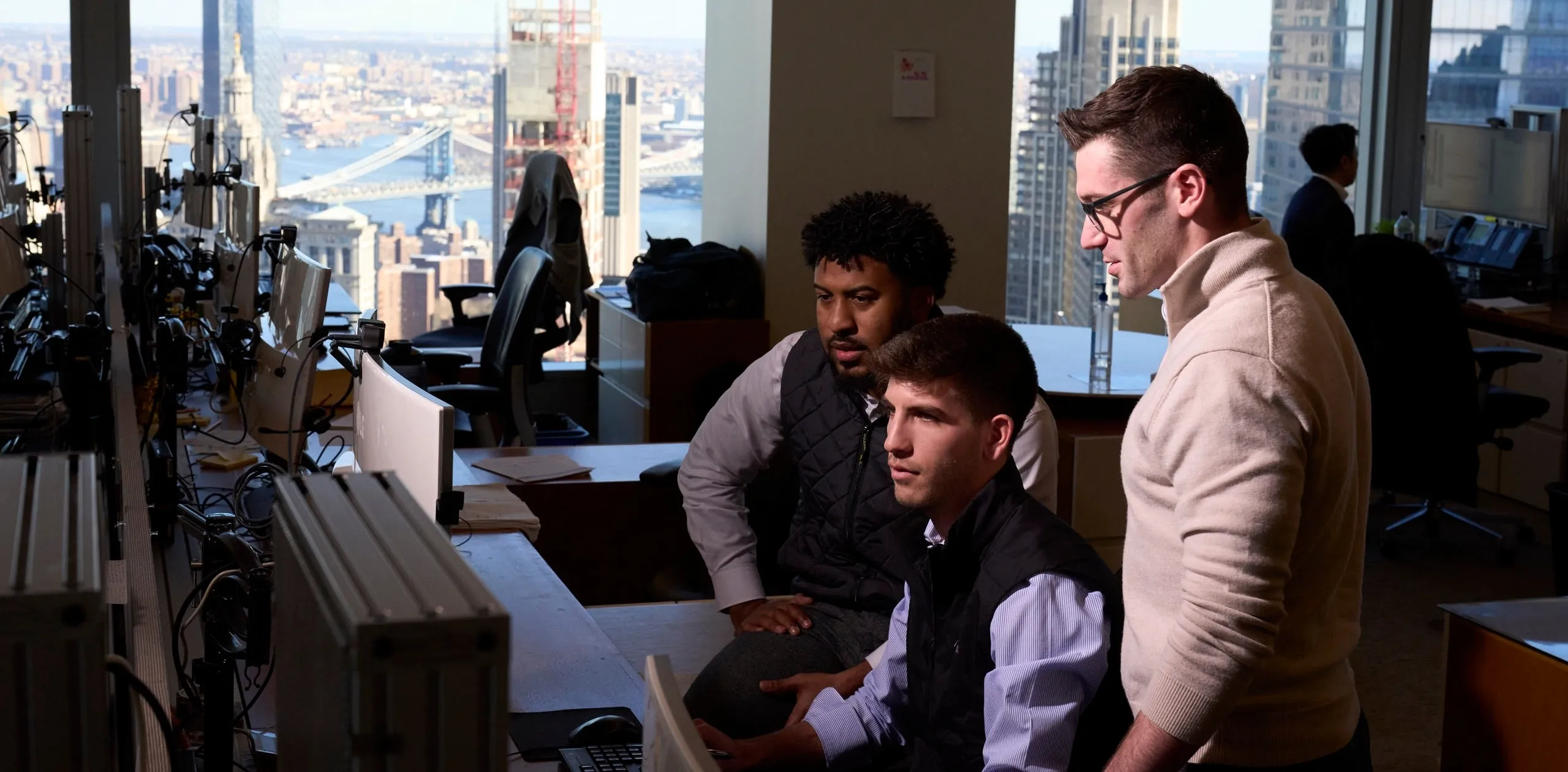 Goldman sachs employees collaborating at office workstations with a city skyline view in the background