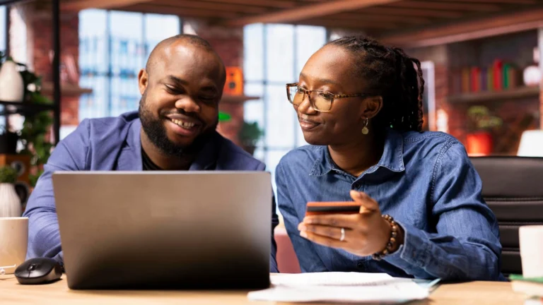 Couple Managing Finances Online Together | Brimco Couple sitting at a desk using a laptop for online banking while holding a credit card