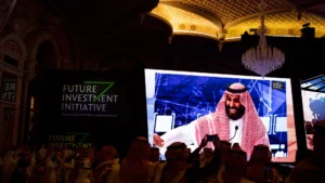 Delegates gathered in riyadh at the future investment initiative with a large screen displaying a keynote speaker in traditional attire