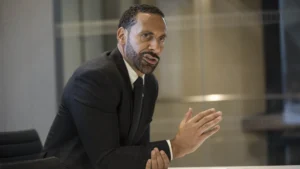 Rio ferdinand in a suit speaking during a meeting gesturing with his hand while making a point
