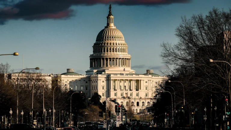 The U.S. Capitol building viewed from Pennsylvania Avenue with cars and pedestrians in the foreground.