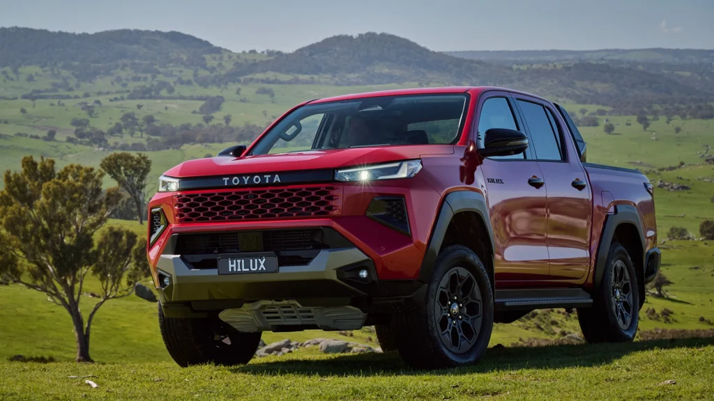 Red toyota hilux pickup truck parked on grassy hills with mountains in the background
