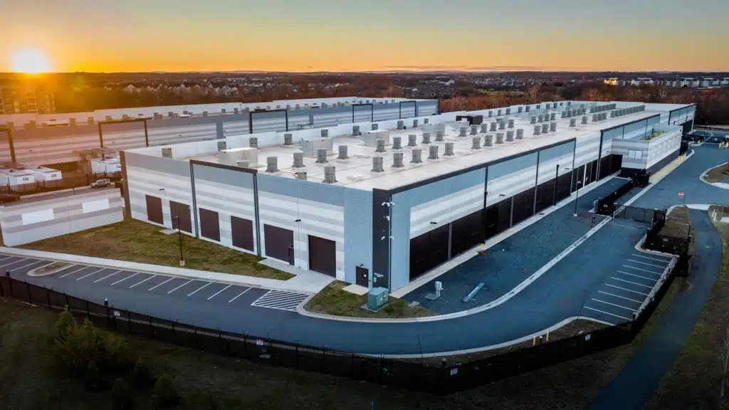 Amazon Data Center at Sunset | Brimco Aerial view of a large amazon data center complex at sunset showing long warehouse style buildings with rooftop cooling units surrounding roads and security fencing