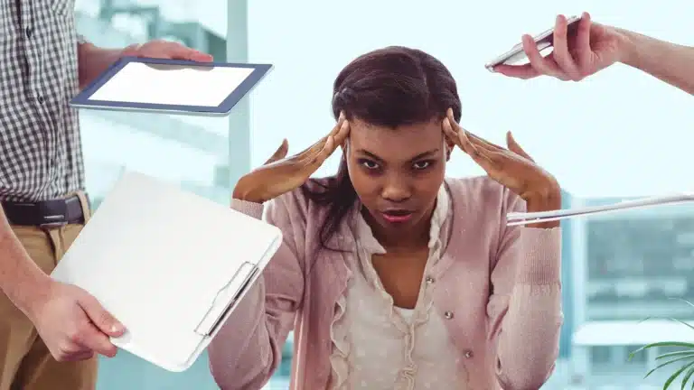 Stressed woman overwhelmed by multiple digital devices and paperwork demanding her attention
