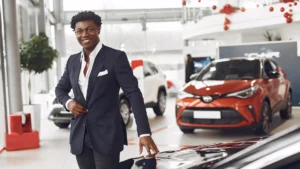 Smiling car sales agent standing in a dealership showroom with new vehicles behind him