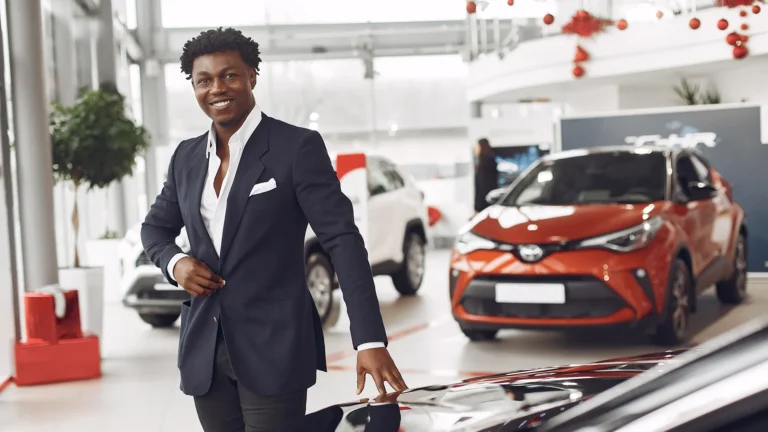Smiling car sales agent standing in a dealership showroom with new vehicles behind him