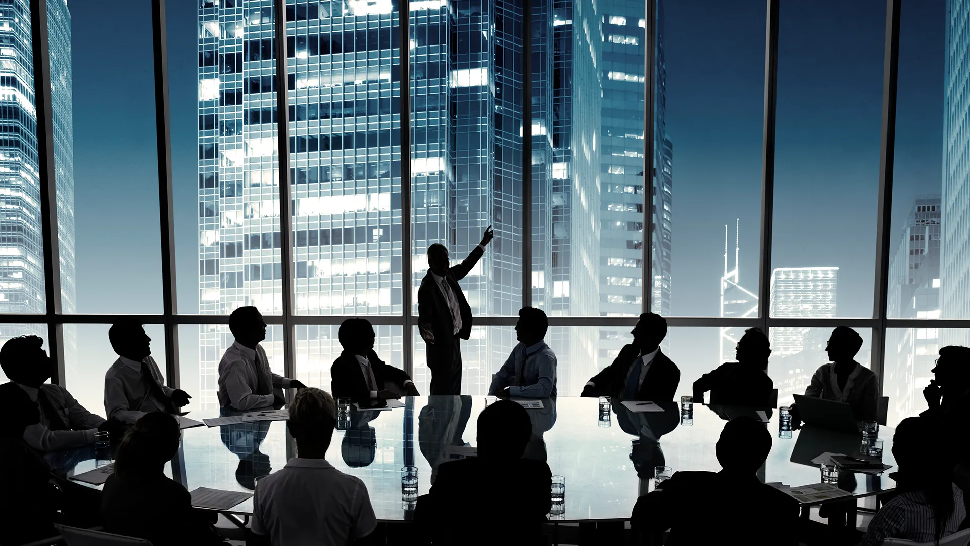 Business leader presenting to a board of executives in a modern high rise conference room overlooking a city skyline at night