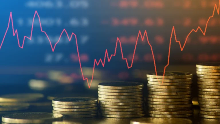 Stacks of coins arranged in increasing height with a red fluctuating line graph over a blurred financial market background.
