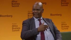 Patrick dlamini wearing a dark suit and red tie speaks onstage at the bloomberg africa business summit against a yellow backdrop