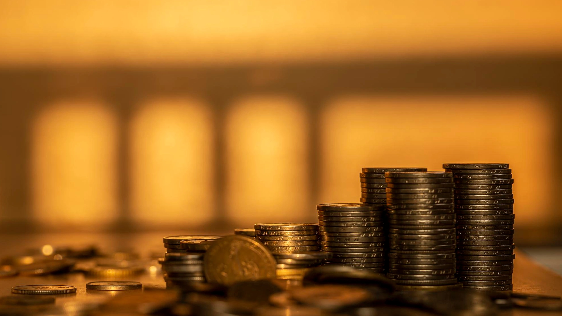 Stacks of Coins Symbolizing Wealth and Financial Growth | Brimco Neatly stacked coins on a table with warm golden lighting representing savings wealth or economic growth