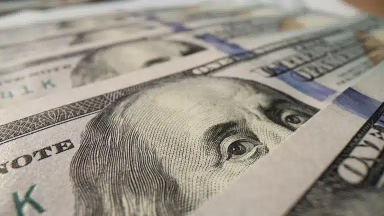 Close-up of US $100 bills featuring Benjamin Franklin’s portrait arranged in overlapping rows.