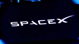 Close-up of the SpaceX logo glowing against a dark background.