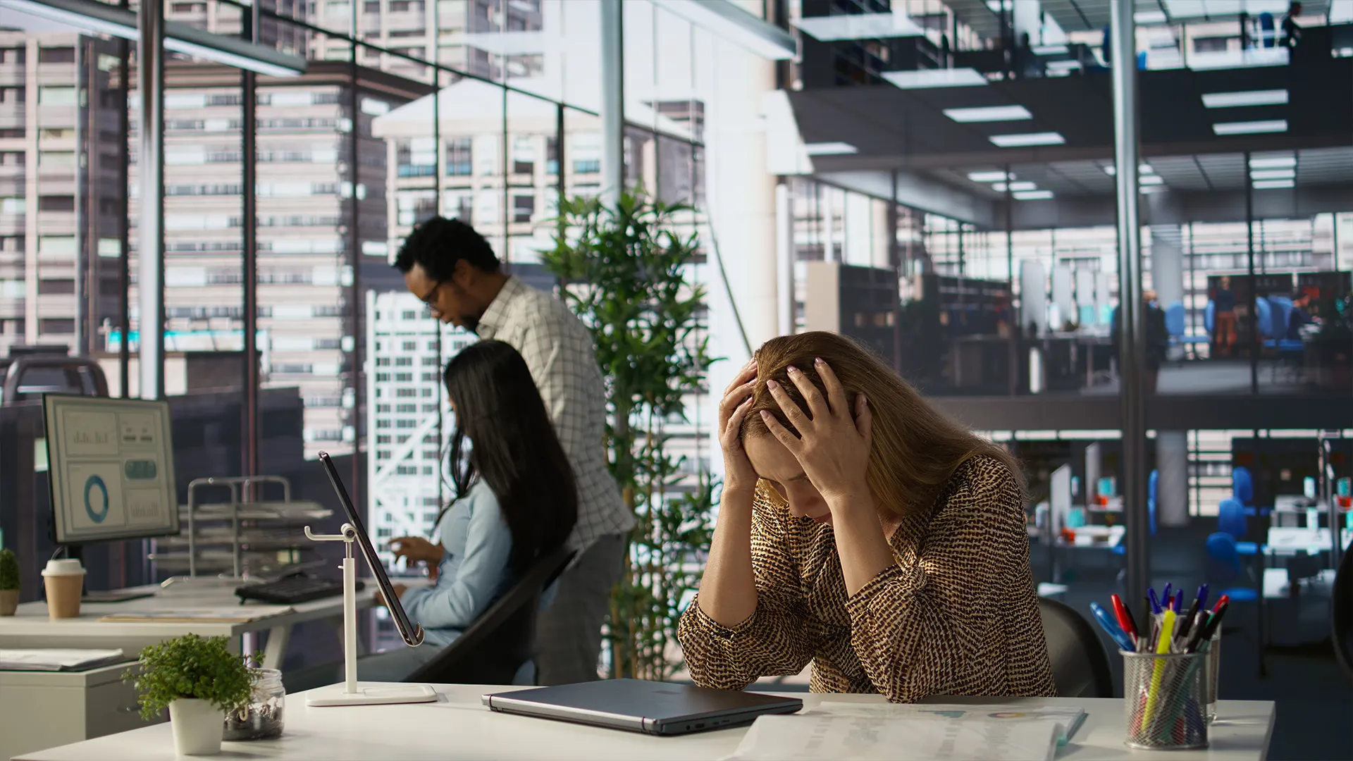Startup Stress and Business Failure Challenges | Brimco Stressed female entrepreneur sitting at a desk in a modern office with hands on her head reflecting startup business challenges